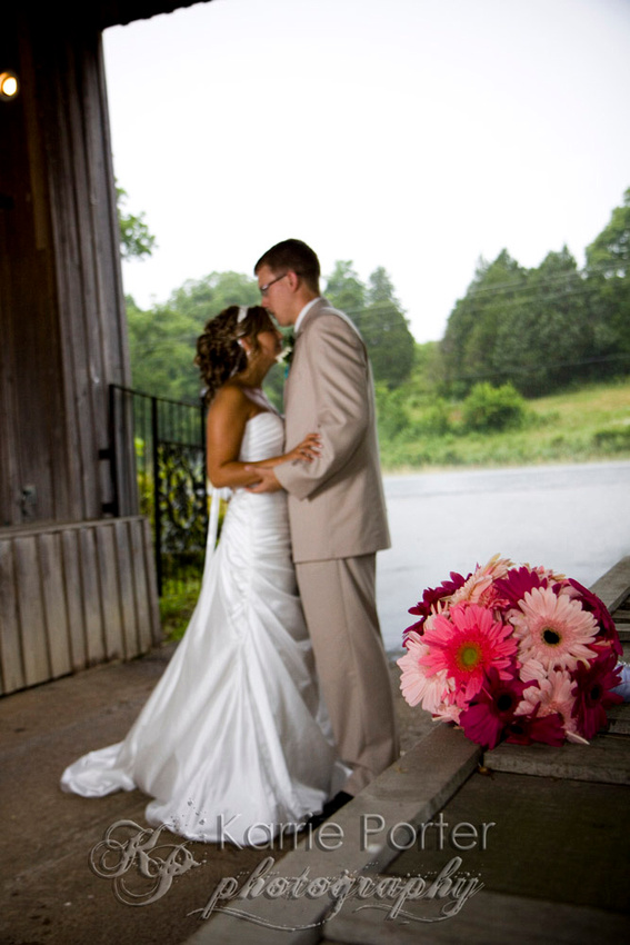 Covered bridge groom kissing bride bouquet in foreground