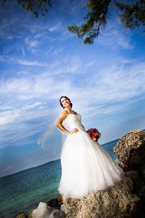 Bride stands on rocks by ocean
