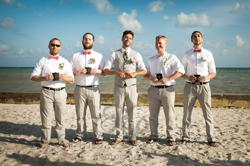 Groomsmen coming out of a Key West wedding on Higgs Beach in their linen slacks and coral bowties, holding custom engraved flasks.